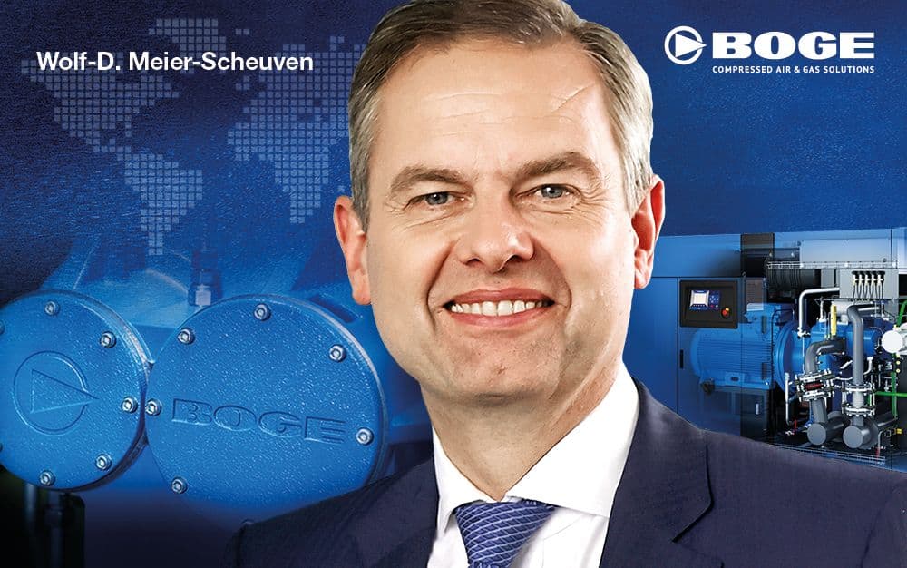 Smiling man in a suit with BOGE branding and industrial equipment in the background.