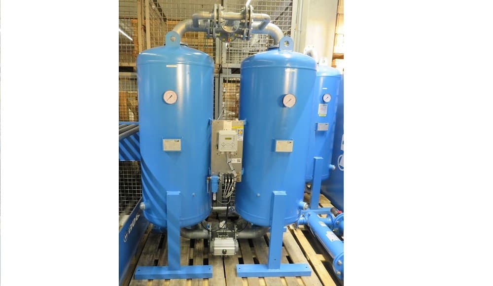 Blue industrial cold-regenerating adsorption dryer with dual receivers and pressure gauges, mounted on a wooden pallet in a warehouse setting.