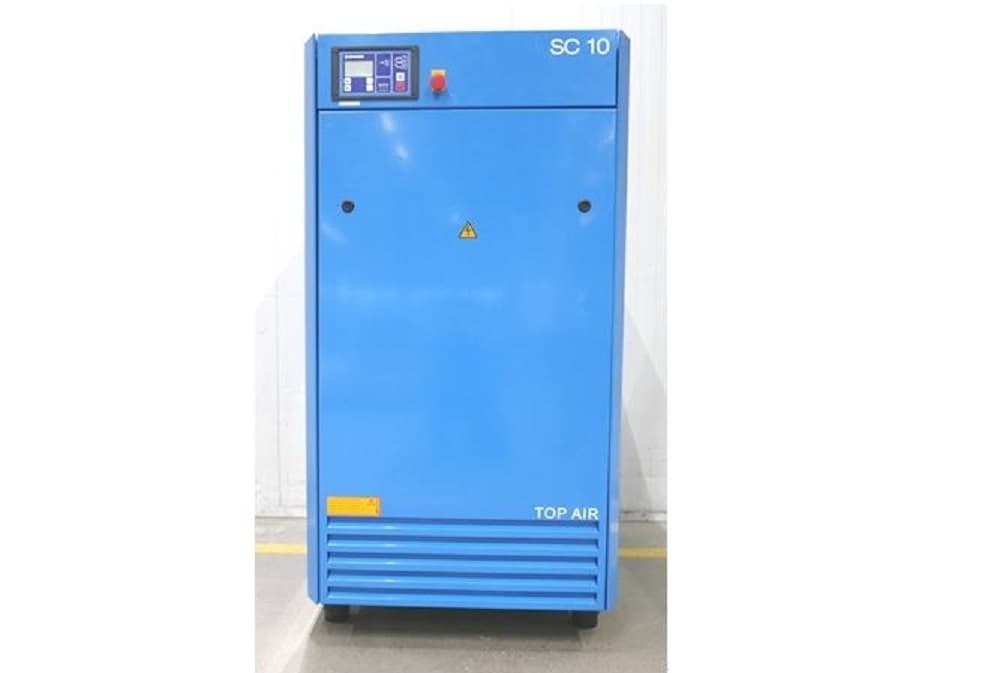 Blue industrial air compressor unit with control panel, labeled "SC 10" and "TOP AIR," standing on a concrete floor.
