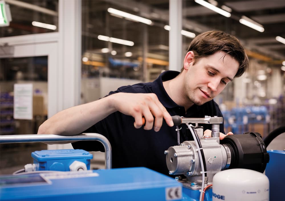 Ein BOGE Servicetechniker schraubt an an einem Kompressor in einer Fabrikhalle.