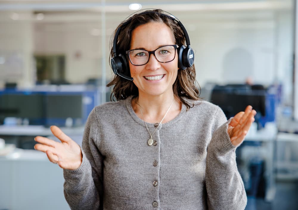 Frau mit Headset guckt laechelnd in die Kamera
