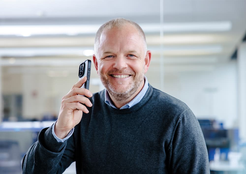BOGE Mitarbeiter lächelt, während er ein Handy in der Hand hält.