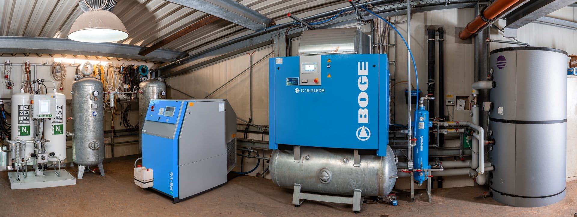Industrial room with BOGE air compressor system, nitrogen generator, and various equipment for compressed air management.
