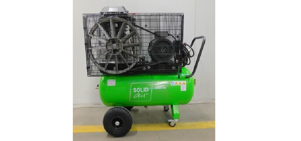 Green portable air compressor with large wheels and protective cage, labeled "Solid Air," positioned against a plain wall.