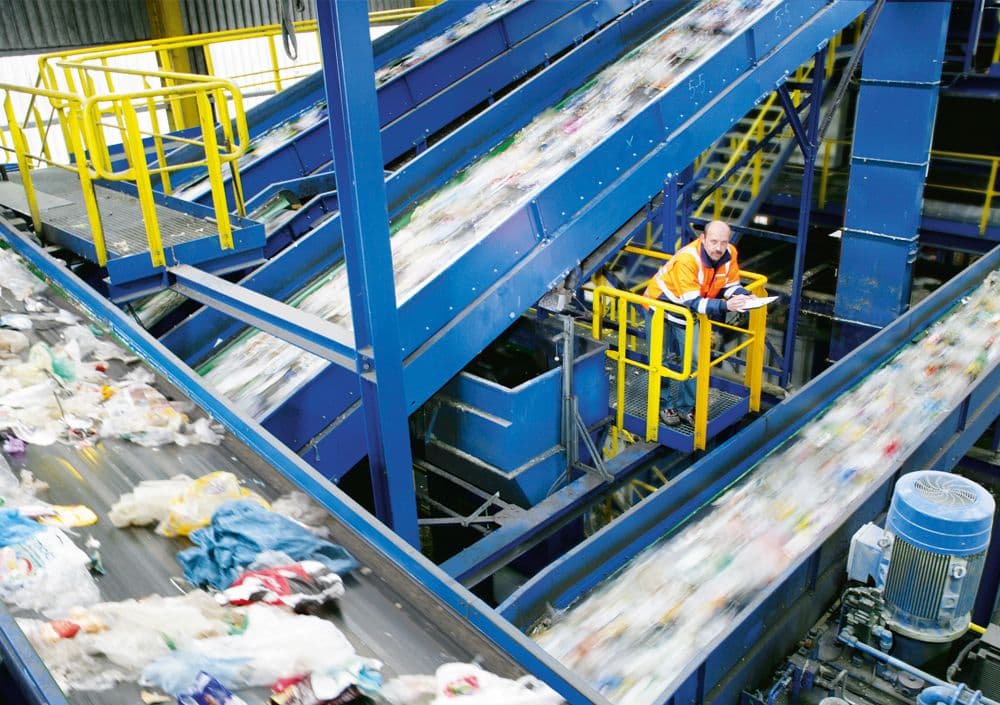 Tönsmeier Mitarbeiter in oranger Warnweste auf einem blauen Gerüst innerhalb einer Mülltrennungsanlage
