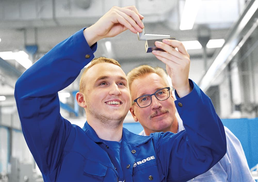 BOGE Azubi begutachtet mit seinem Ausbilder ein Bauteil welches er in der Hand misst