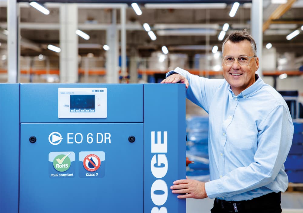 BOGE Gebrauchtmaschinen Ansprechpartner Thomas Wenzel steht lächelnd neben einem Kompressor der EO Baureihe