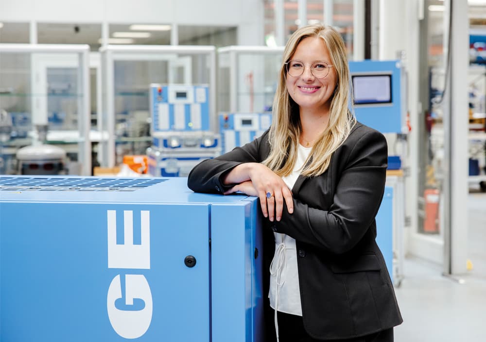 Julia Meier-Scheuven, Business Development Managerin der fünften Inhabergeneration bei BOGE Kompressoren, steht in der Produktion am Standort Bielefeld neben einem BOGE Druckluftkompressor.