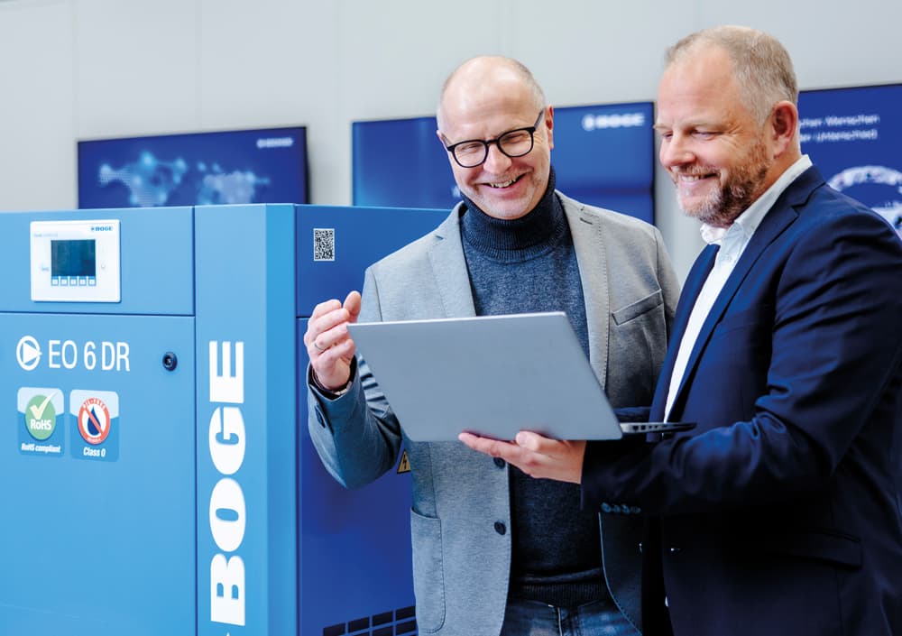 Kunde und BOGE Berater im freundlichen Gespräch mit Laptop in der Hand neben einem blauen Scrollkompressor