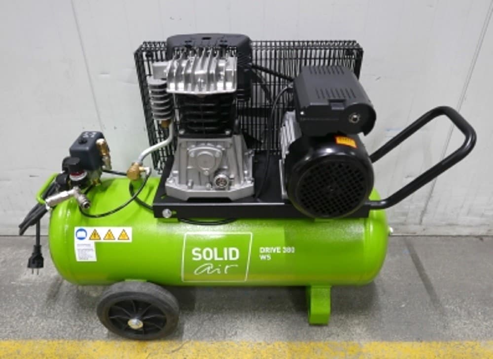 Green portable air compressor with a black motor, labeled "SOLID air," on wheels, positioned on a concrete floor.