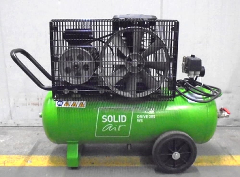 Green air compressor with protective cage, mounted on wheels for mobility, labeled "SOLID air DRIVE 899 WS," in an industrial setting.