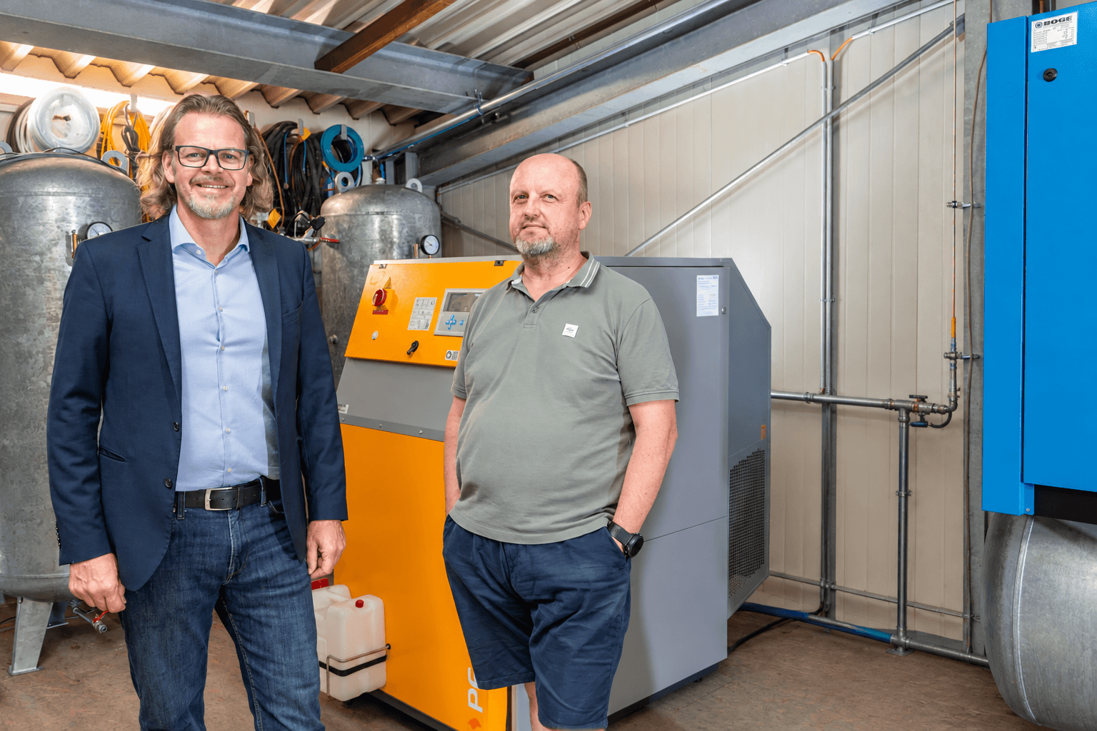 Two men standing in an industrial setting with BOGE air compressors and equipment in the background.