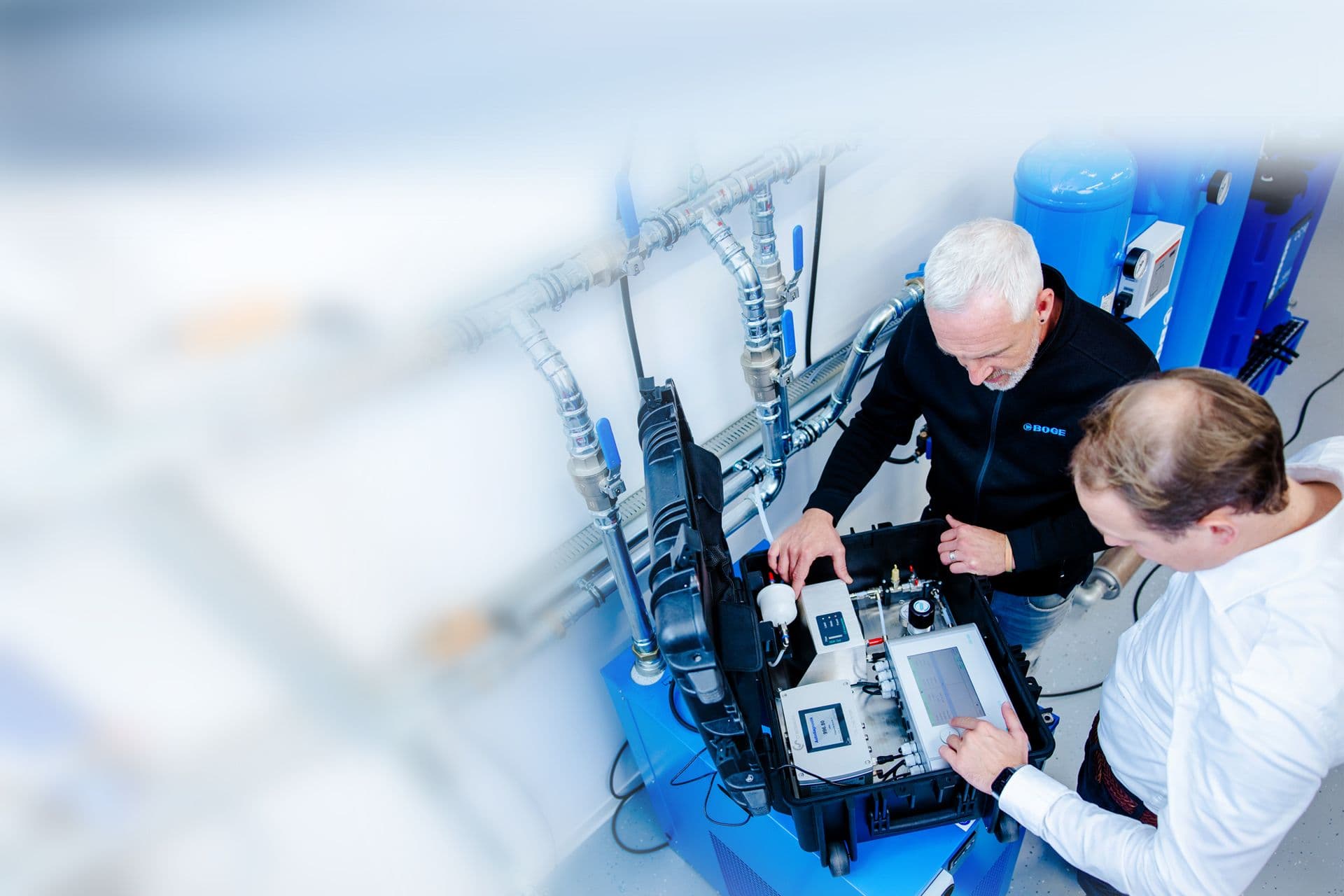 Zwei BOGE Mitarbeiter stehen vor einem Druckluftsystem und messen die Qualitaet