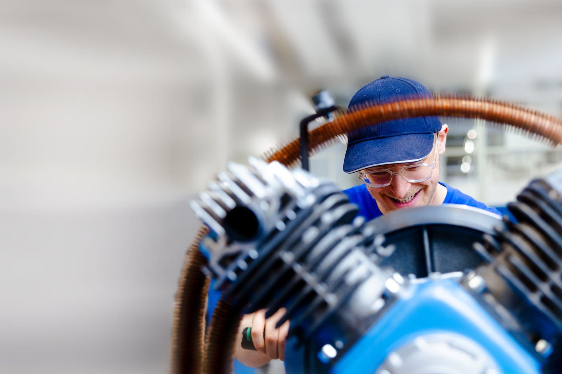 Ein lachender BOGE Mitarbeiter schraubt an einem blauen Kompressor