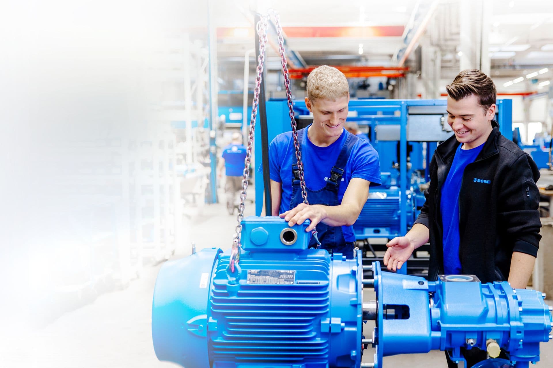 Zwei BOGE Monteure stehen an kranmontiertem Kompressorbauteil und betrachten die Motoreinheit.