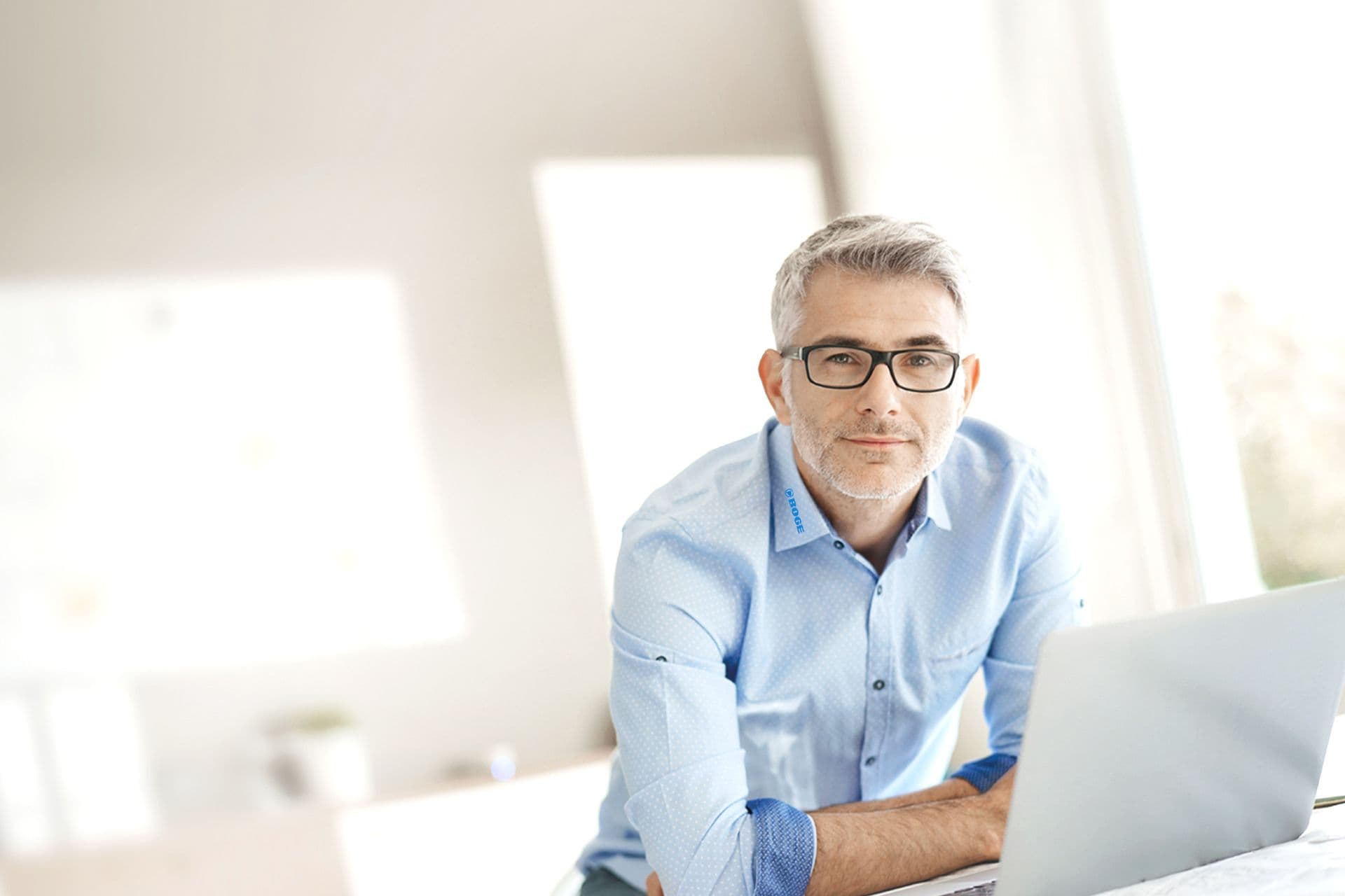 Ein Boge Mitarbeiter aus der Verwaltung steht einem Laptop am Arbeitsplatz und guckt in die Kamera