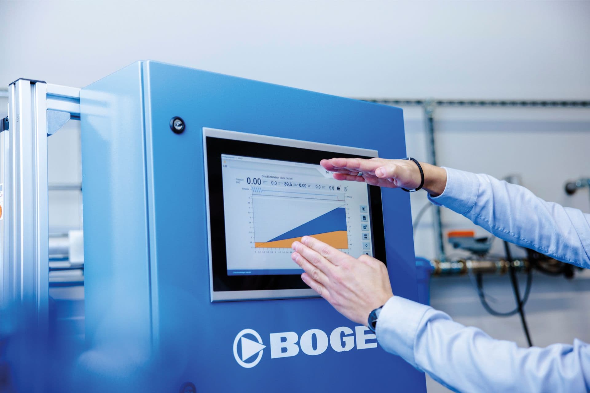 Person, die mit einem Touchscreen interagiert, auf dem ein Liniendiagramm auf einer blauen BOGE-Maschine in einer industriellen Umgebung angezeigt wird.