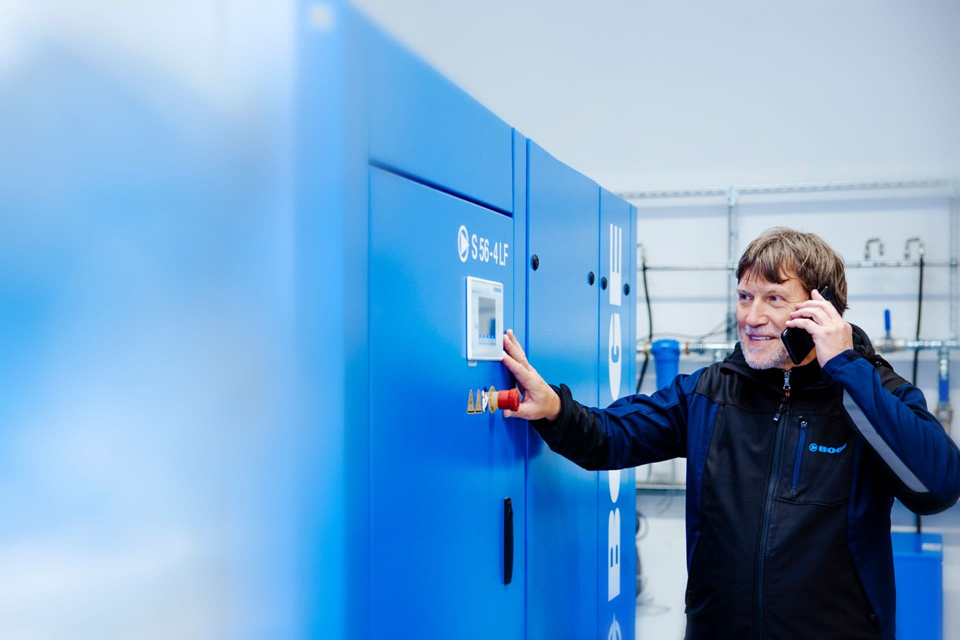 Ein BOGE Mitarbeiter steht vor einem Schraubenkompressor und telefoniert mit einem Kunden