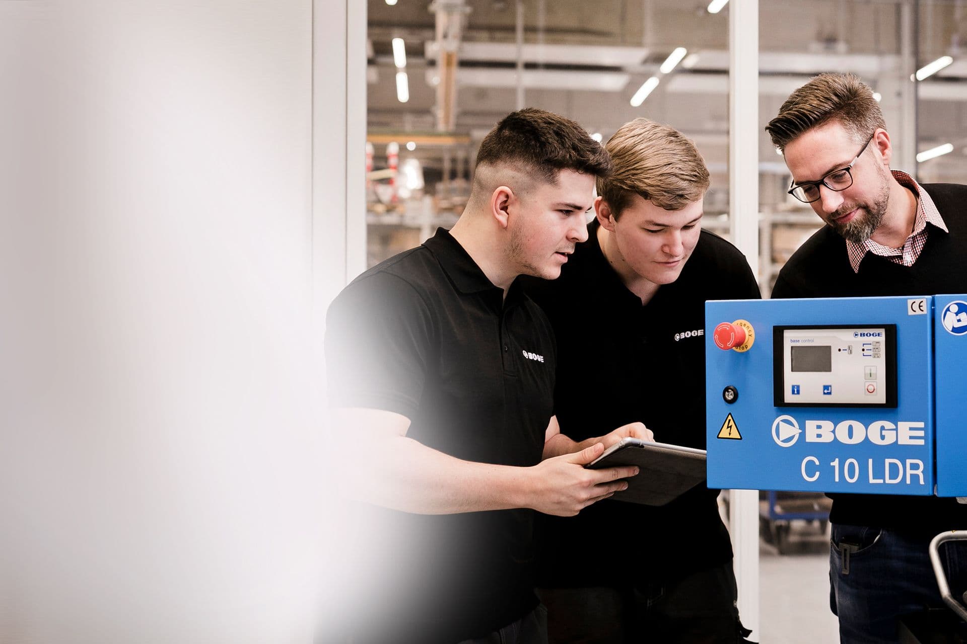 BOGE Azubis halten ein Tablet in der Hand und stehen mit ihrem Ausbilder vor einem geöffneten Kompressor der C-Baureihe