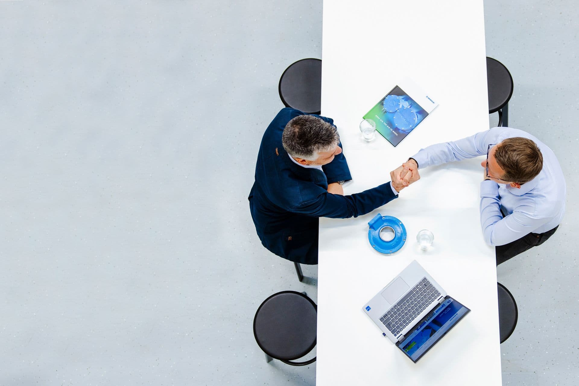 Zwei BOGE Mitarbeiter sitzen an einem Tisch und besprechen Unterlagen und Laptop aus der Vogelperspektive.