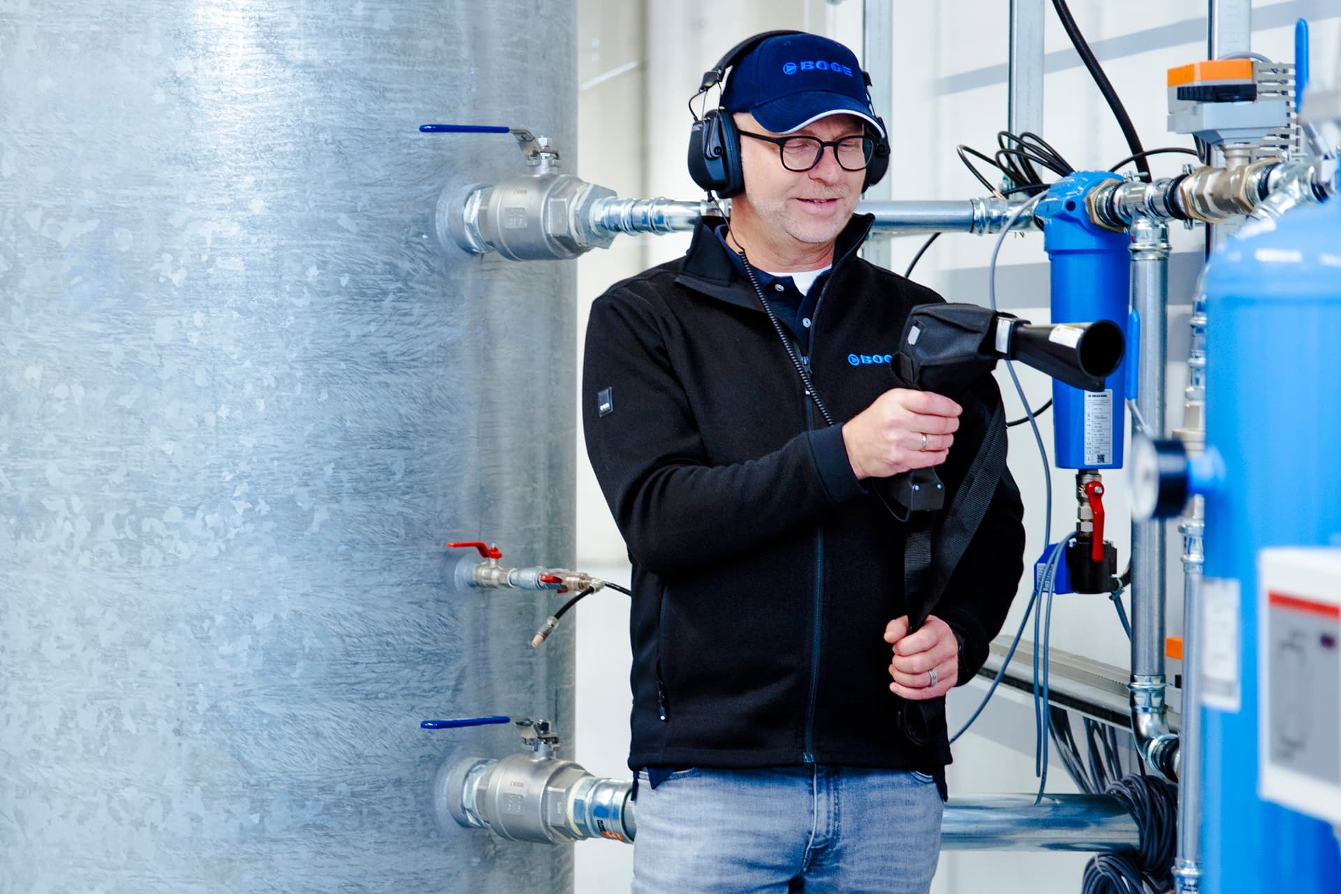BOGE servicetechniker steht bei einer Druckluftanlage und schaut auf sein Messgerät, während einer Druckluftmessung.