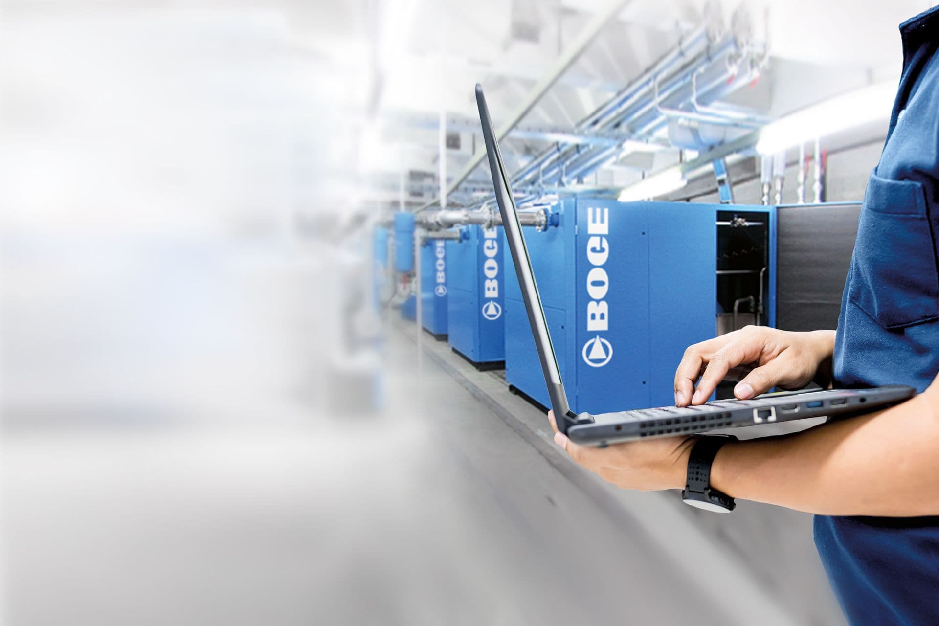 Ein BOGE Mitarbeiter steht mit seinem Laptop vor einer ganzen Reihe von BOGE Kompressoren und schaut auf sein Laptop, ob die Kompressoren laufen