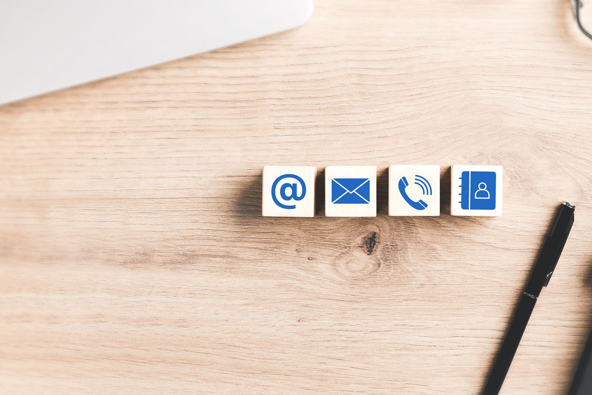 Würfel mit Kontaktmöglichkeiten auf einem hellbraunen Holzschreibtisch daneben ein schwarzer Stift