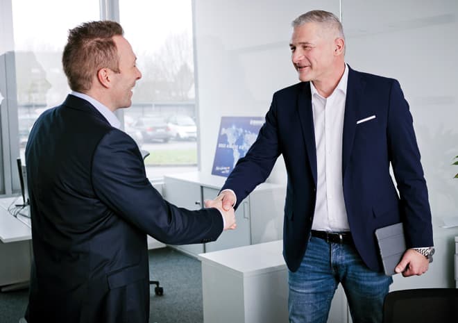 BOGE Finanzierungsberater schüttelt einem Kunden bei einem Beratungsgespräch die Hand und hält ein Tablet in der Hand