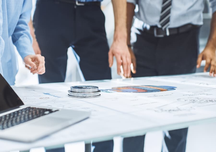 Drei Mitarbeiter Besprechen eine Zeichnungsunterlage auf einem Tisch.